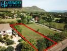 Aerial view of a land plot outlined in red, bordering a road with a scenic backdrop of mountains and houses