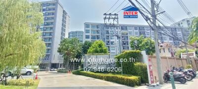 Modern residential apartment building under clear blue skies with lush greenery and real estate signage