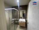 Modern bathroom with shower and glass door, featuring marble walls and wooden vanity