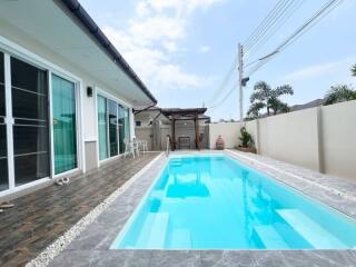 Spacious outdoor pool area next to a modern house with large sliding doors and a clear sky