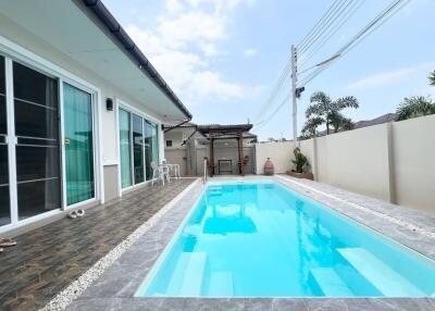 Spacious outdoor pool area next to a modern house with large sliding doors and a clear sky