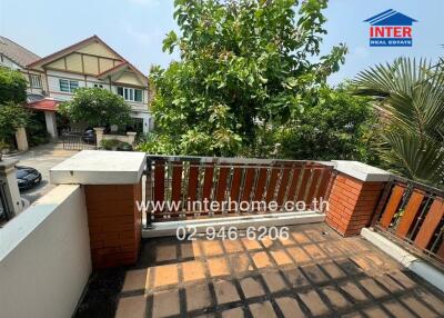 View from the outdoor balcony showing a tiled floor, brick railing, and lush greenery with neighboring houses