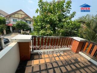 View from the outdoor balcony showing a tiled floor, brick railing, and lush greenery with neighboring houses