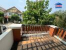 View from the outdoor balcony showing a tiled floor, brick railing, and lush greenery with neighboring houses