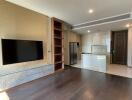 Modern living room with open kitchen design, featuring a large flat-screen TV and dark wooden flooring