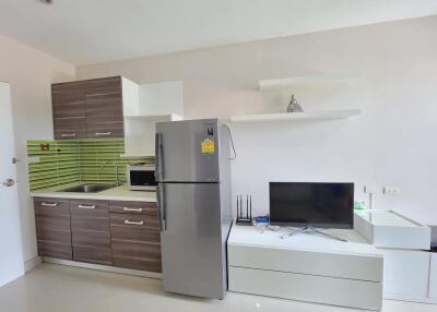 Modern kitchen with integrated living room space featuring stainless steel refrigerator, TV, and wooden cabinets