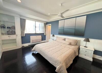Spacious and elegantly furnished bedroom with dark hardwood floors and serene blue walls