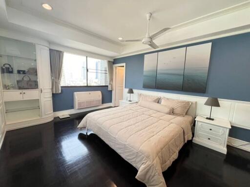 Spacious and elegantly furnished bedroom with dark hardwood floors and serene blue walls