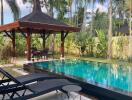 Luxurious backyard with a swimming pool, sun loungers, and a gazebo amidst lush greenery