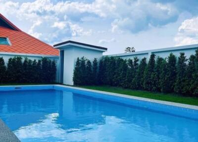 Modern residential outdoor swimming pool beside a house with a red tiled roof under a clear blue sky