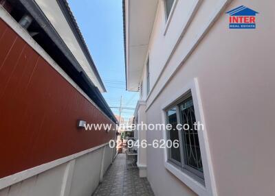 Narrow alleyway between residential buildings with visible exterior details and a clearly marked real estate sign