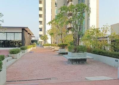 Spacious outdoor common area with seating and greenery between residential buildings