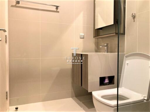 Modern bathroom interior with beige tiles, featuring a toilet, shower area, and washbasin with storage