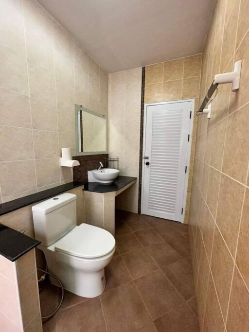 Modern bathroom with tiled floors and walls featuring sink, toilet, and door