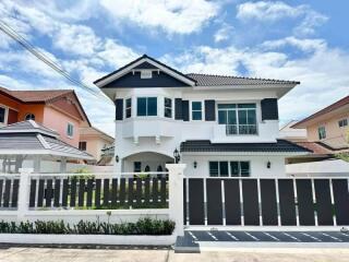 Modern two-story house with white exterior and grey roof, featuring a balcony and a secure fence