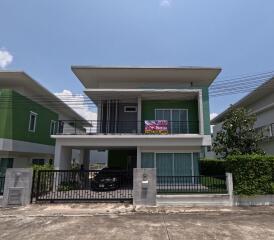 Two-story house with a for sale sign, surrounded by green painted walls, under a blue sky