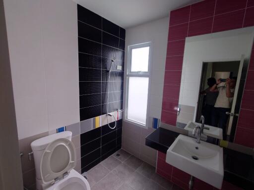 Spacious modern bathroom with black and pink tiles, featuring a large mirror, sink, and toilet