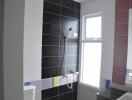 Modern bathroom with black tiled shower area, large window, and white fixtures