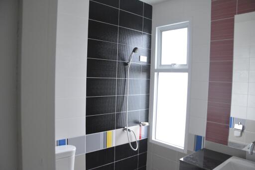 Modern bathroom with black tiled shower area, large window, and white fixtures