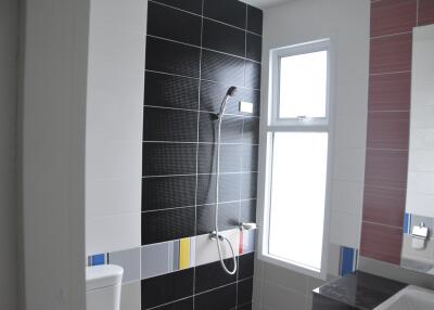 Modern bathroom with black tiled shower area, large window, and white fixtures