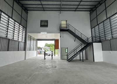 Spacious industrial building interior with high ceiling and stairs leading to a lofted office area