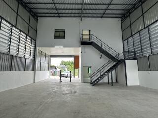 Spacious industrial building interior with high ceiling and stairs leading to a lofted office area