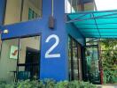 Modern blue two-story building entrance with large number 2, greenery, and a sleek glass awning