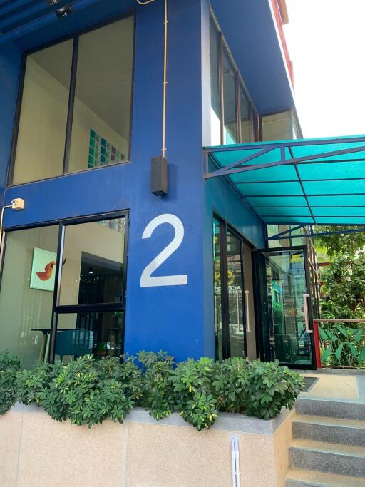 Modern blue two-story building entrance with large number 2, greenery, and a sleek glass awning