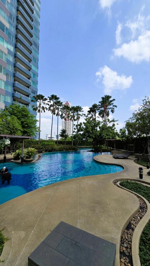 Luxurious outdoor swimming pool surrounded by lush gardens and modern high-rise buildings
