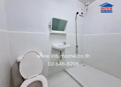 Compact white tiled bathroom with toilet, sink, and shower
