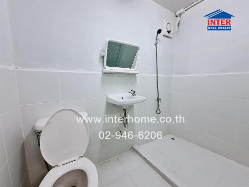 Compact white tiled bathroom with toilet, sink, and shower