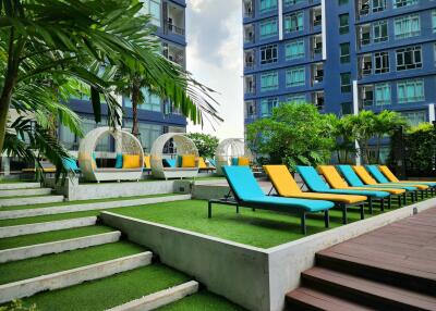 Modern apartment complex with vibrant outdoor leisure space featuring colorful lounge chairs and lush greenery