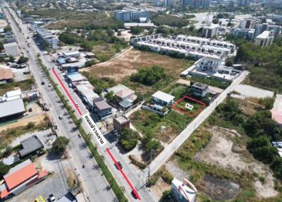 Aerial view of a property plot marked in red near a main road surrounded by residential and commercial buildings