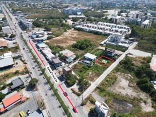 Aerial view of a property plot marked in red near a main road surrounded by residential and commercial buildings