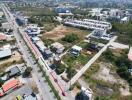 Aerial view of a property plot marked in red near a main road surrounded by residential and commercial buildings