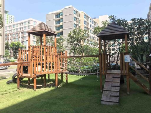 Spacious outdoor common area with wooden play structures and lush greenery in a residential apartment complex