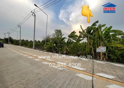 Paved road with real estate signage and lush greenery under a clear sky