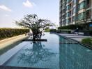 Luxurious outdoor swimming pool with reflective water and a decorative tree, surrounded by modern residential buildings