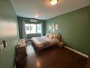 Cozy and well-lit bedroom with green walls and hardwood flooring