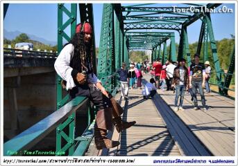 Person costumed as a pirate sitting on a metal bridge with pedestrian traffic in the background