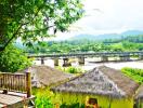 Scenic view of thatched huts and a bridge over a river with mountains in the background