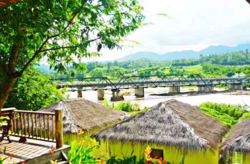 Scenic view of thatched huts and a bridge over a river with mountains in the background