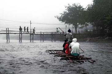 Misty river scene with people crossing on a bridge and a raft