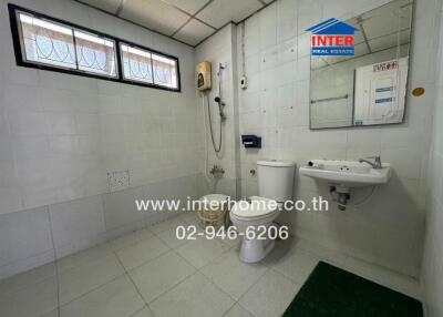 Spacious and clean bathroom with tiled walls and flooring, equipped with toilet, sink, and large window for natural light