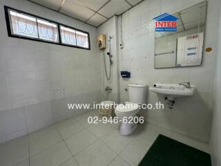 Spacious and clean bathroom with tiled walls and flooring, equipped with toilet, sink, and large window for natural light