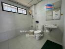 Spacious and clean bathroom with tiled walls and flooring, equipped with toilet, sink, and large window for natural light