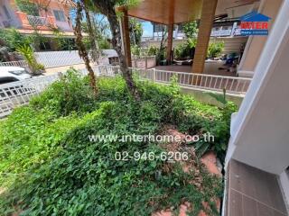 Spacious outdoor area with lush greenery and a covered carport nearby