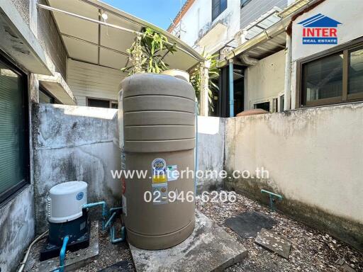 Outdoor utility area with large water storage tank and plumbing fixtures