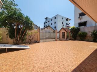 Spacious outdoor area with terracotta tiles and lush greenery surrounding a gated property