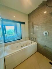 Modern bathroom with bathtub and shower near a large window overlooking greenery